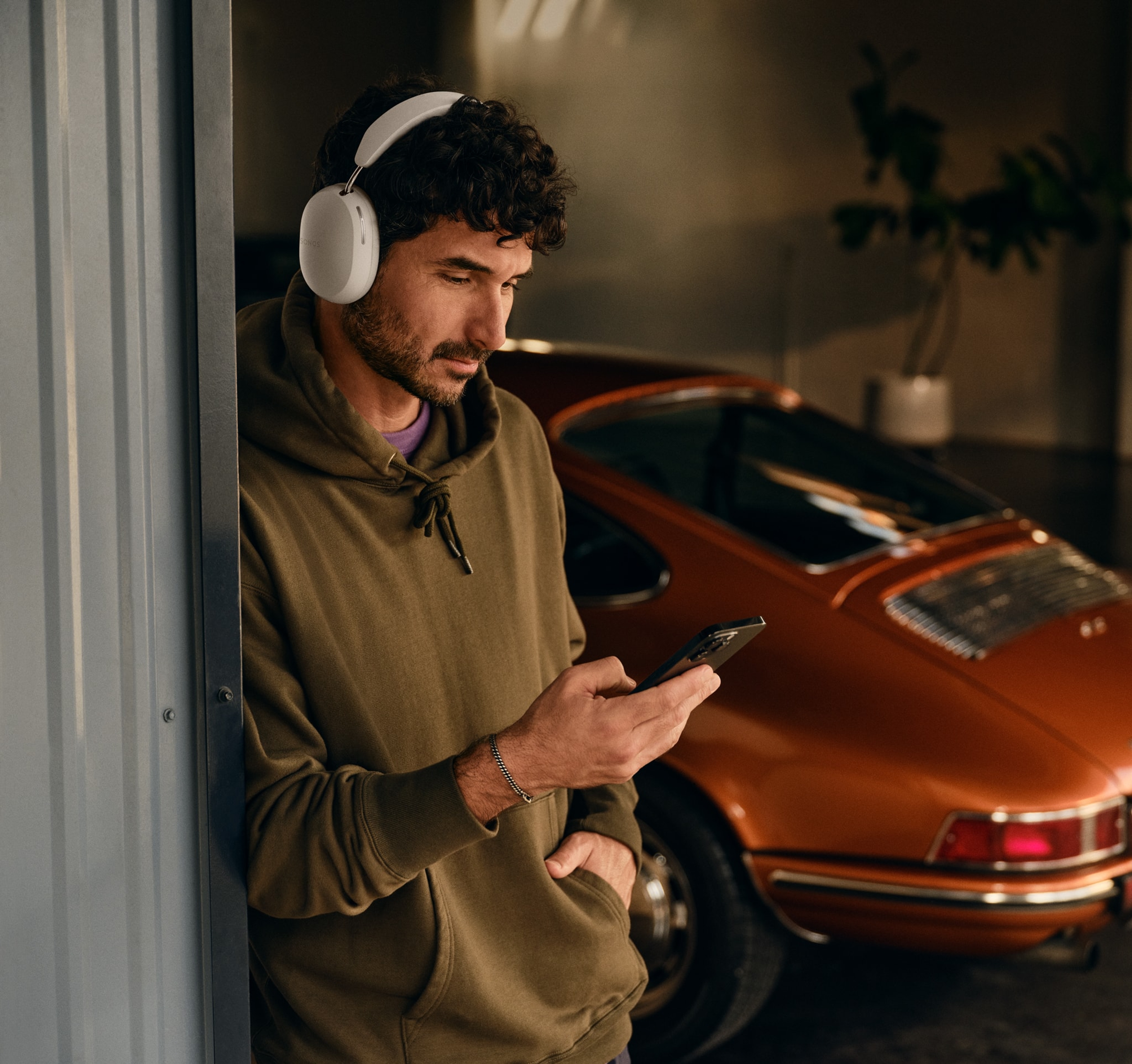 Una persona accanto a una macchina indossa le cuffie Sonos Ace bianche mentre usa il telefono