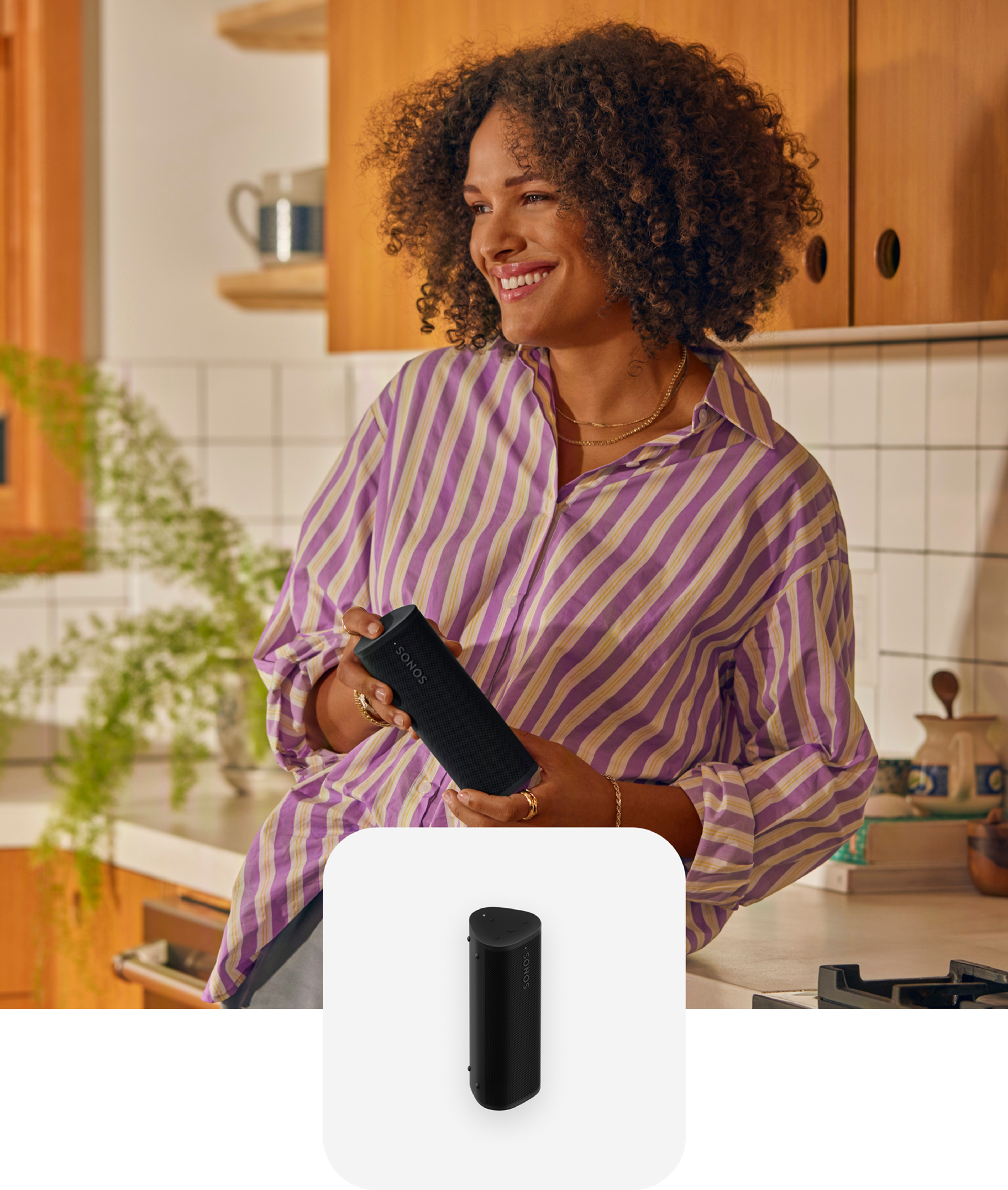 Una mujer sostiene una bocina portátil Roam 2 en color negro mientras escucha música en la cocina