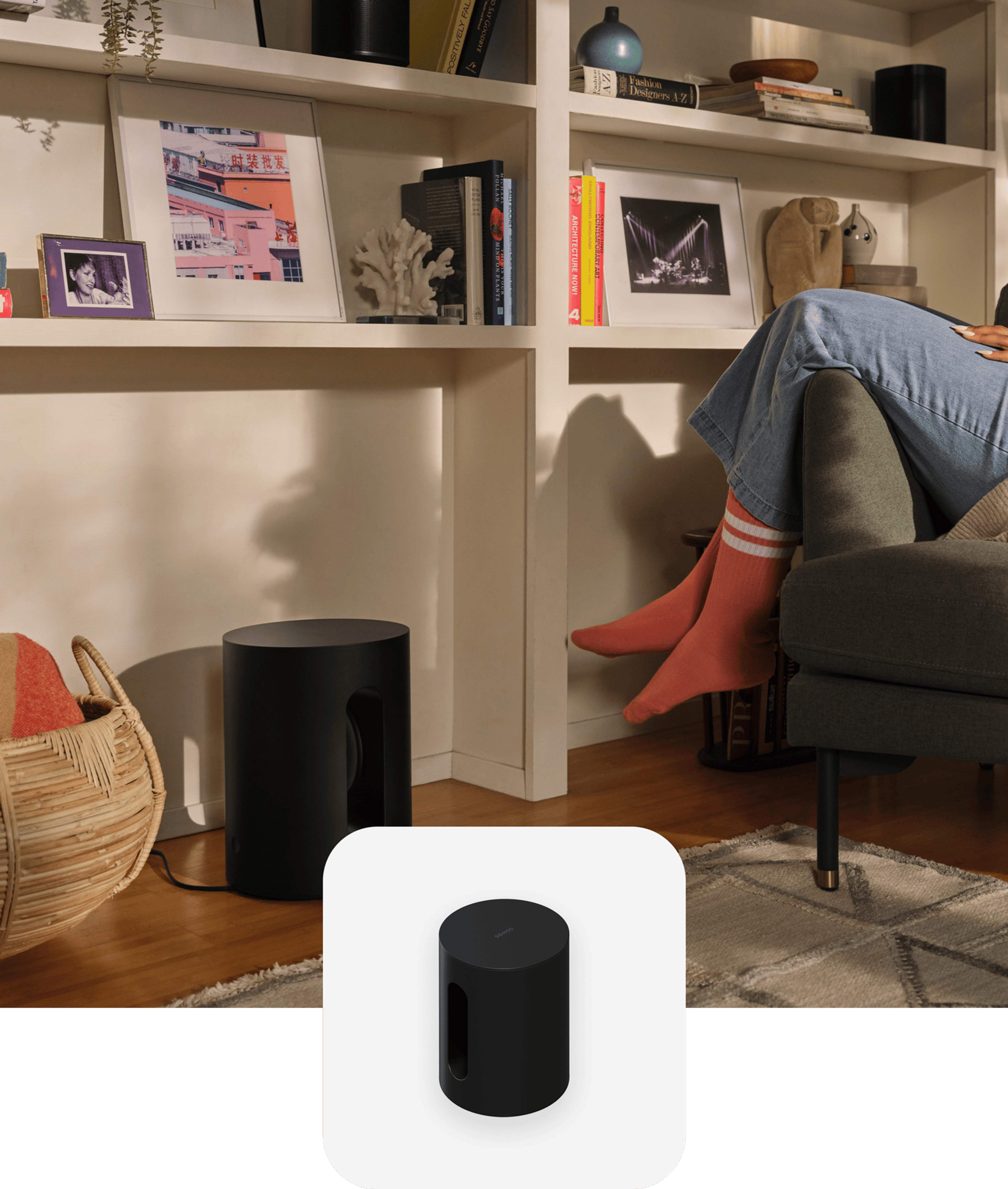 Una persona sentada en un sillón en la sala junto a un Sonos Sub Mini en color negro