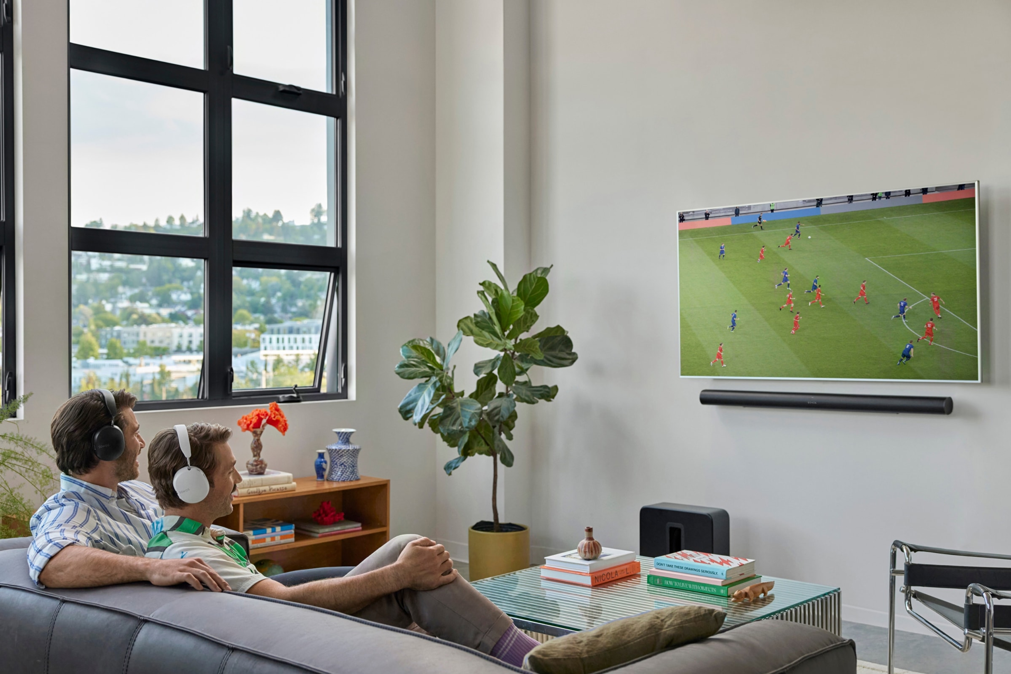 Familj som sitter i soffan och tittar på tv med en svart Arc Ultra och en svart Sub 4