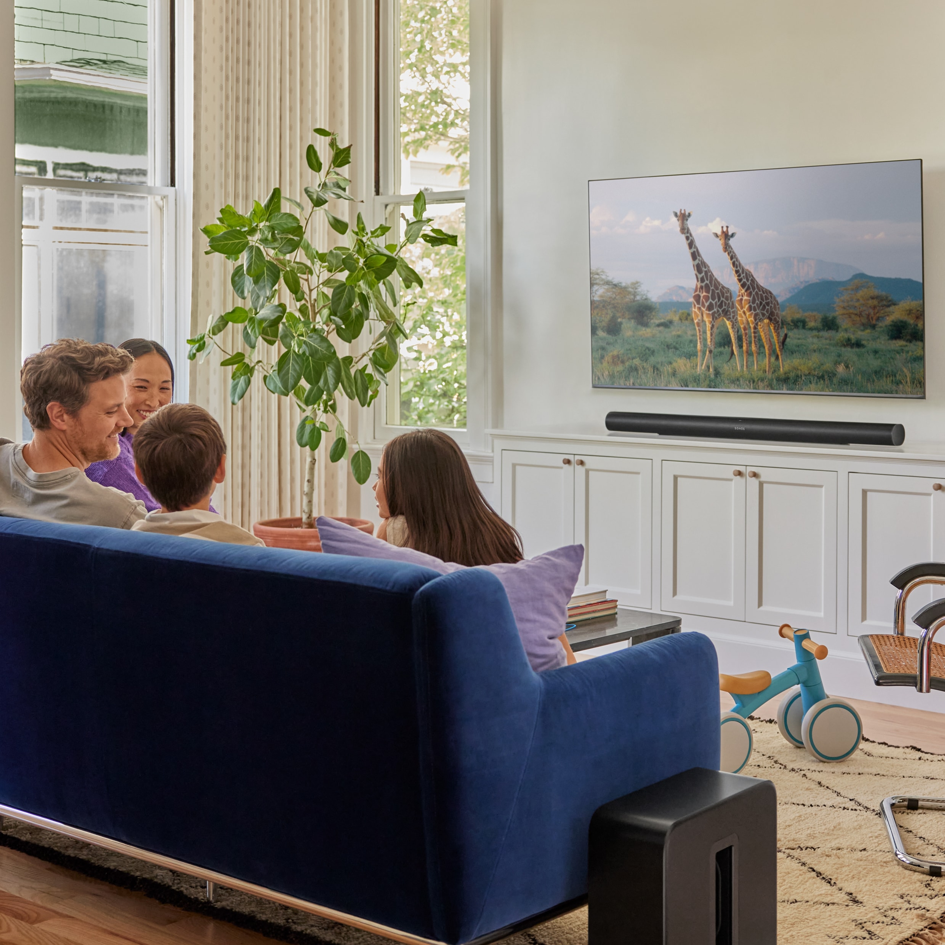 En familie i en sofa ser på TV med en svart Arc Ultra og en svart Sub 4
