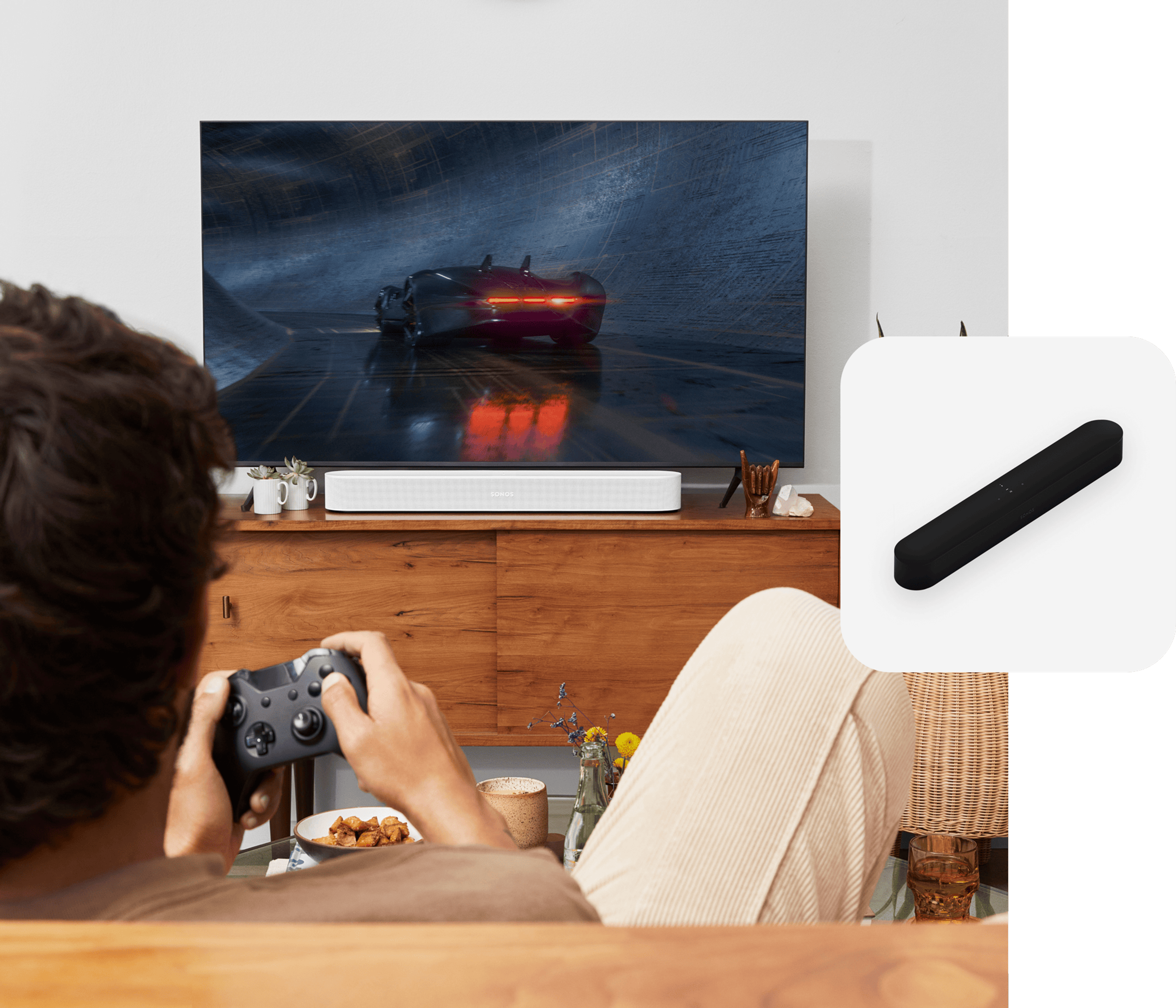 Un usuario juega en un sofá mientras el audio se reproduce en una barra de sonido Sonos Beam en color blanco