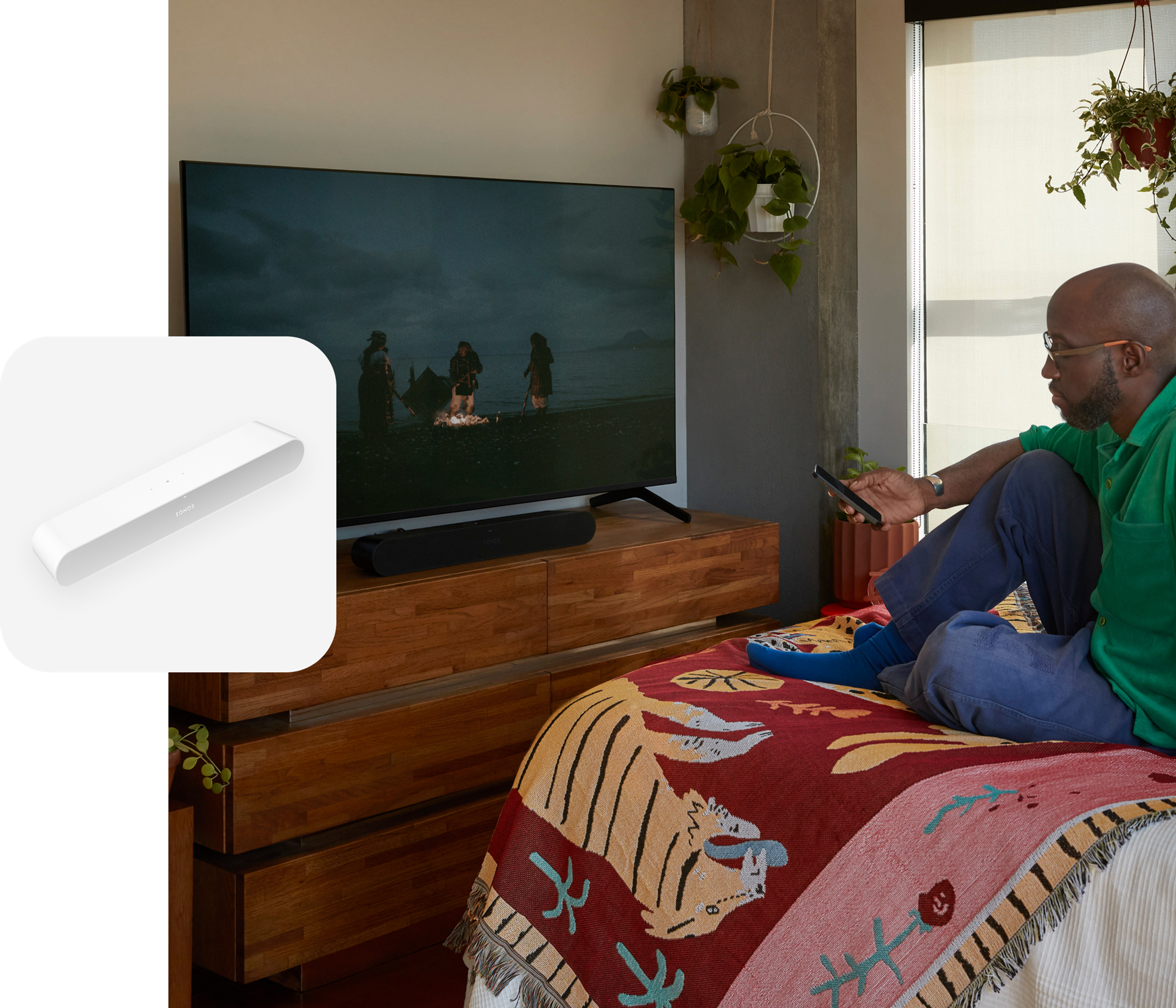 Una persona sentada en una cama mira una película con el sonido de una barra de sonido Ray en color negro