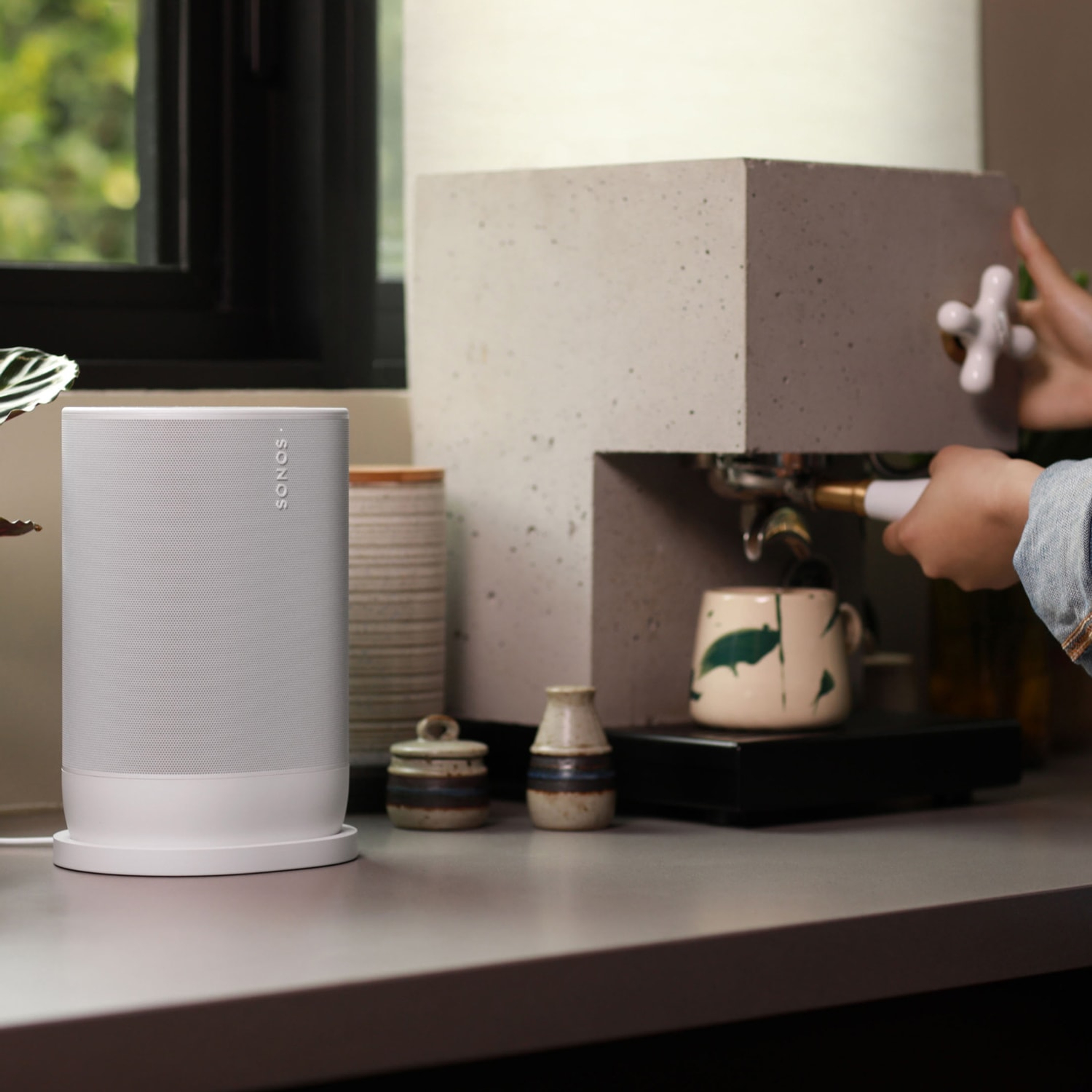 Kuva naisesta valmistamassa espressoa keittiön työtason ääressä valkoisen Sonos Move 2:n vieressä